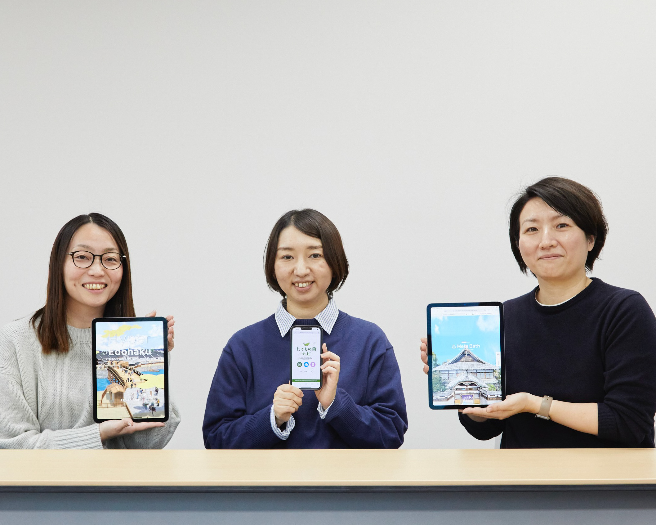 From left to right: Kumiko Fukui, Minako Taguchi, and Manae Kobayashi. The tablets and smartphone display, from left to right: the Edo-Tokyo Museum’s smartphone app Hyper Edohaku, the web app Edo-Tokyo Open Air Architectural Museum Map & Guide, and the museum’s online exhibition Meta Bath ~A digital view of a Tokyo-style bathhouse~