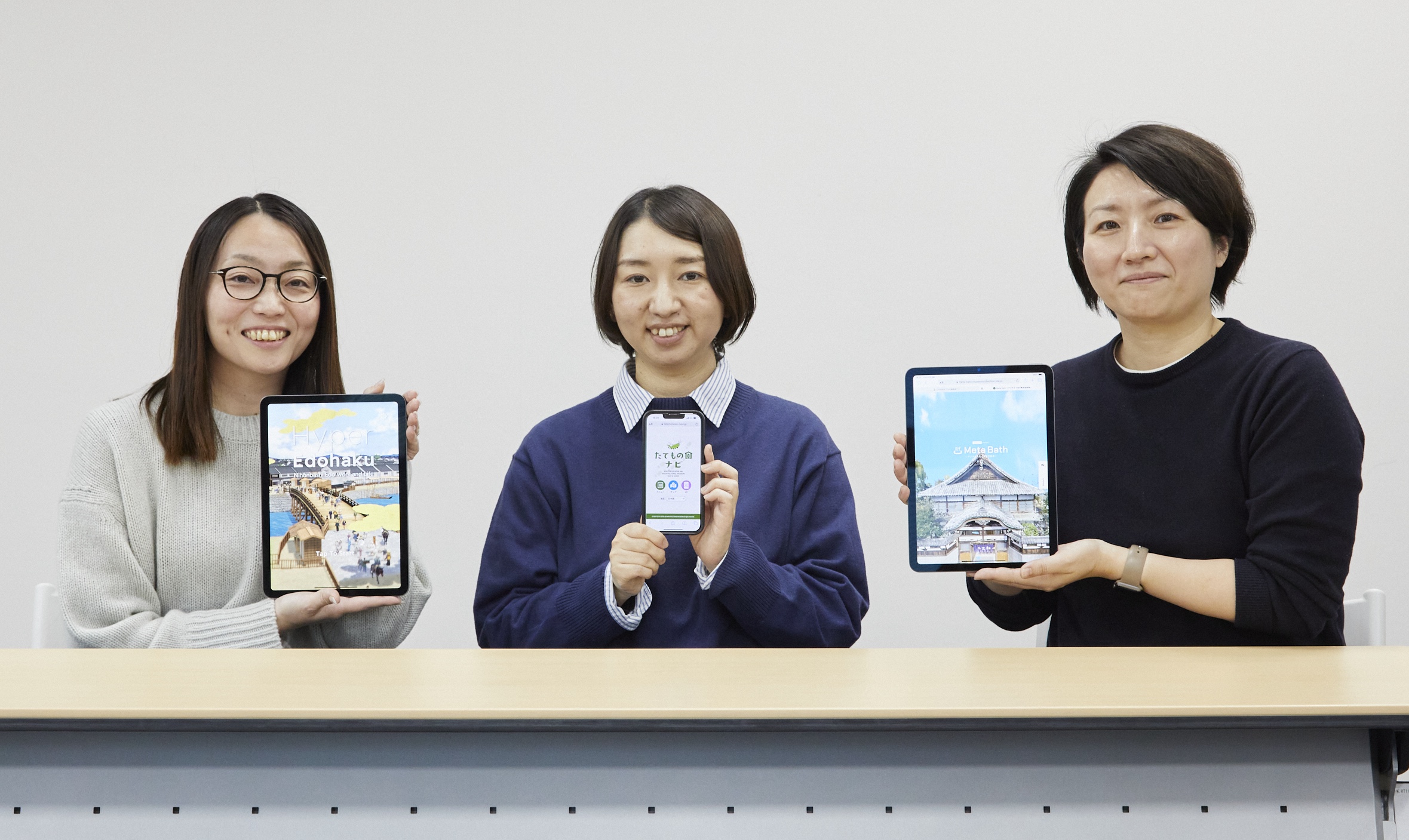 左から福井久美子さん、田口充奈子さん、小林愛恵さん。手元のタブレットとスマートフォンに表示しているのは、左から江戸東京博物館のスマートフォンアプリ「ハイパー江戸博」、江戸東京たてもの園のウェブアプリ「たてもの園ナビ」、同館のオンライン展覧会「Meta Bath（メタバス）～デジタルで見る東京型銭湯～」