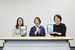 左から福井久美子さん、田口充奈子さん、小林愛恵さん。手元のタブレットとスマートフォンに表示しているのは、左から江戸東京博物館のスマートフォンアプリ「ハイパー江戸博」、江戸東京たてもの園のウェブアプリ「たてもの園ナビ」、同館のオンライン展覧会「Meta Bath（メタバス）～デジタルで見る東京型銭湯～」